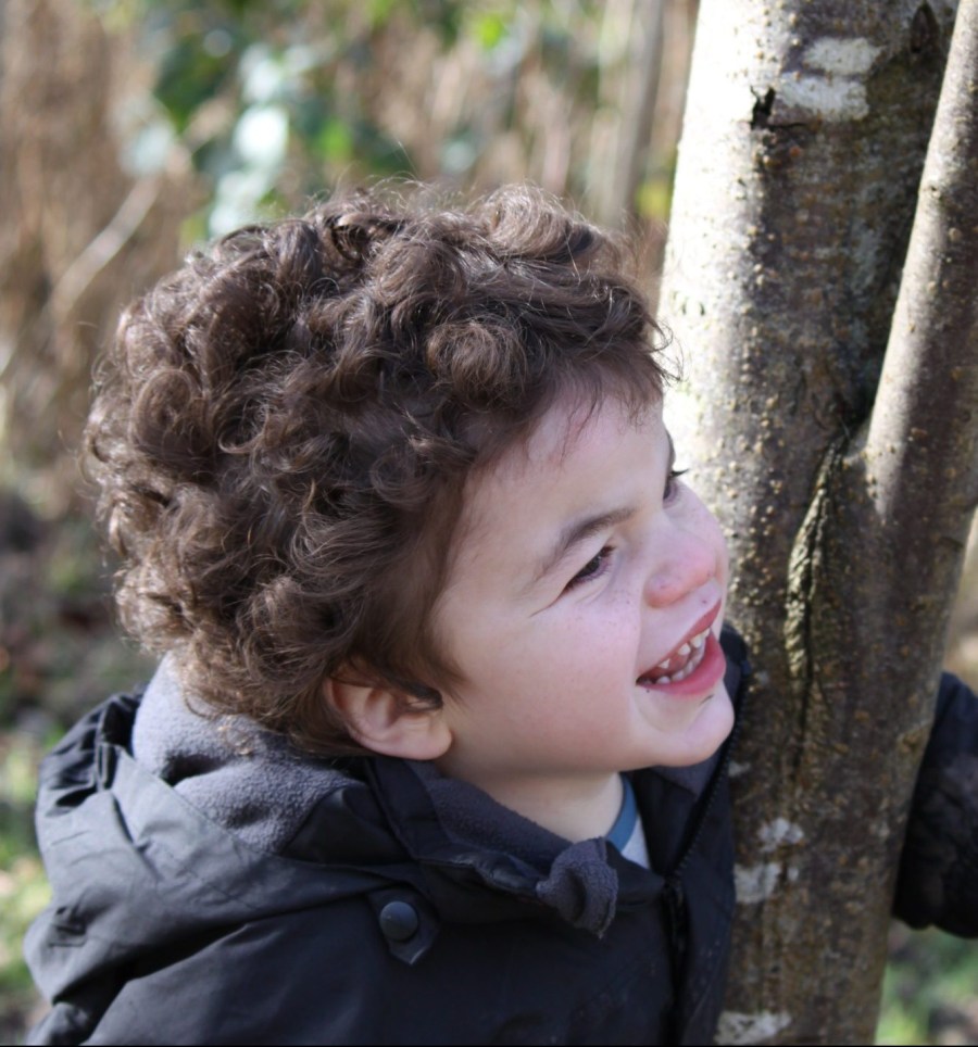 Pudding peering around a tree with a huge cheeky grin.
