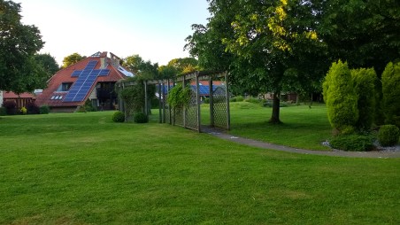 A path winding through some trees and under a pergola. Hospice buildings in the background.